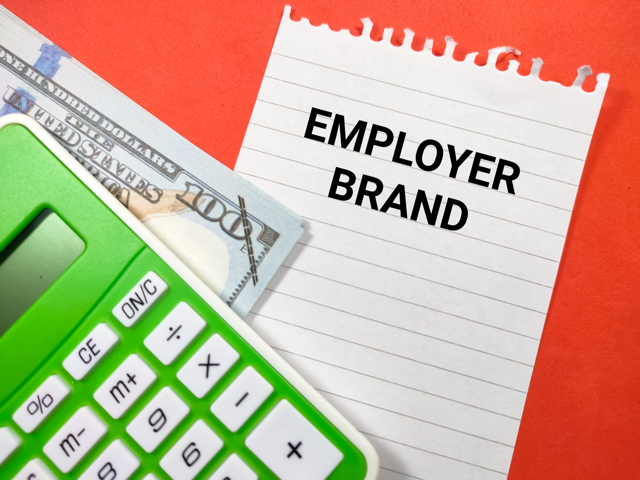 Zeleni kalkulator, novčanica od 100 dolara i bilješka s natpisom "EMPLOYER BRAND" na narančastoj pozadini.