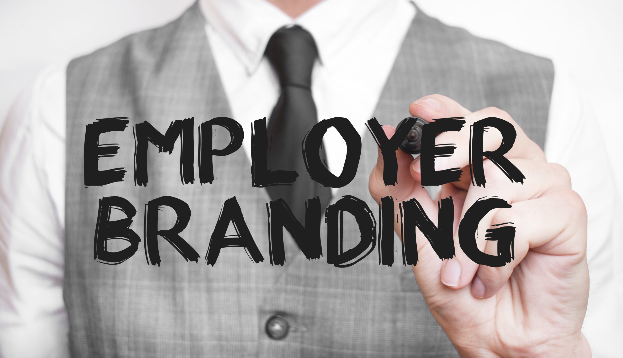 Ruka muškarca u poslovnoj odjeći s markerom u ruci, piše riječi "EMPLOYER BRANDING" velikim slovima na prozirnoj pozadini.